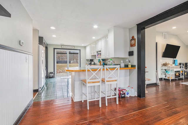 kitchen with dark wood-type flooring, a breakfast bar, visible vents, white cabinets, and freestanding refrigerator