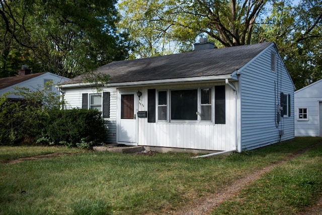 view of front facade with roof with shingles, a chimney, and a front lawn