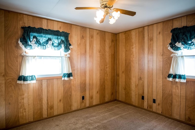 carpeted empty room featuring ceiling fan, wood walls, and baseboards