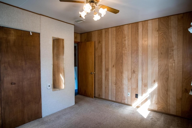 unfurnished bedroom with carpet, wooden walls, visible vents, and a ceiling fan