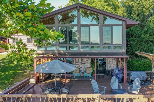 back of house with a deck, stone siding, outdoor dining area, and a sunroom