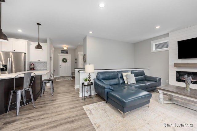 living area with baseboards, light wood-type flooring, a fireplace, and recessed lighting