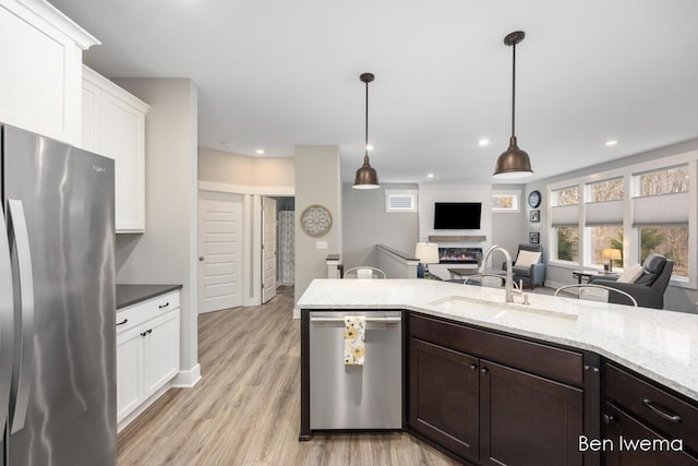 kitchen with dark brown cabinetry, a sink, open floor plan, appliances with stainless steel finishes, and a glass covered fireplace