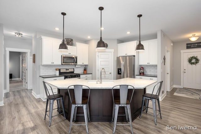 kitchen with appliances with stainless steel finishes, a sink, a center island with sink, and white cabinets