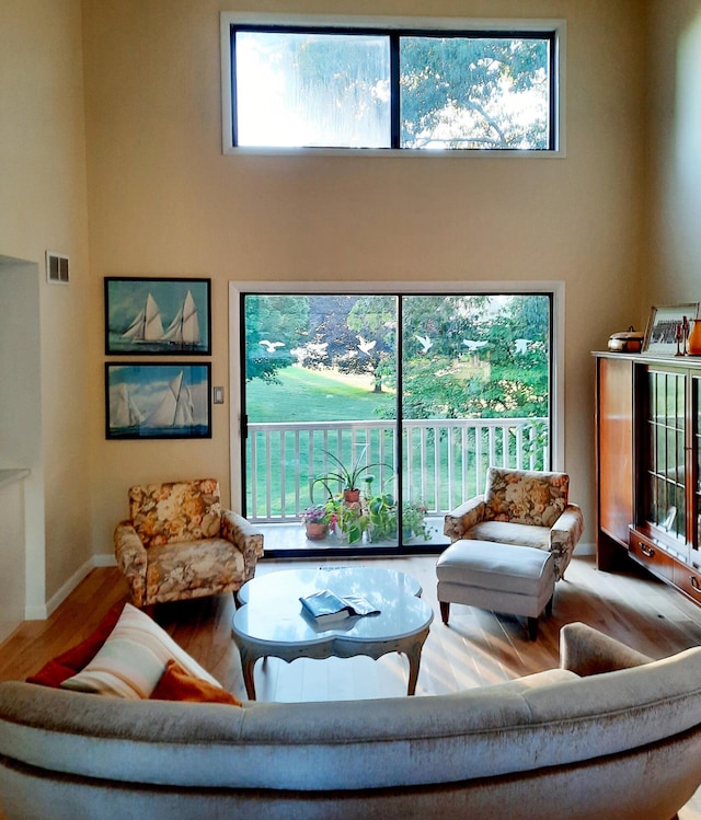 living area featuring a healthy amount of sunlight, a high ceiling, visible vents, and wood finished floors