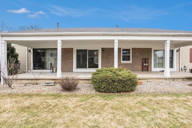 back of house with roof with shingles, a porch, a lawn, and brick siding