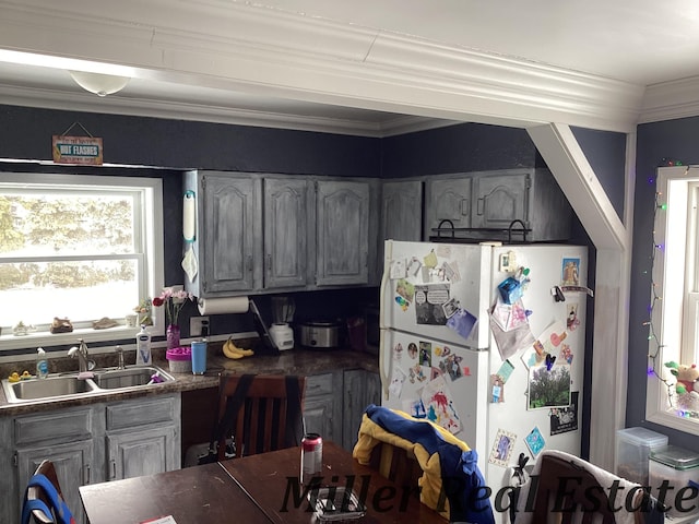 kitchen with dark countertops, a sink, freestanding refrigerator, and crown molding