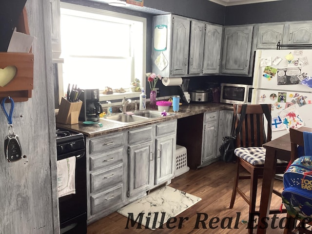 kitchen with dark wood finished floors, stainless steel microwave, black gas range oven, freestanding refrigerator, and a sink