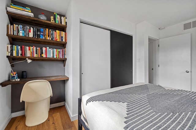 bedroom with a closet, visible vents, baseboards, and wood finished floors