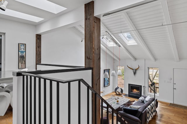 living room featuring wood finished floors, lofted ceiling with skylight, and a fireplace with flush hearth