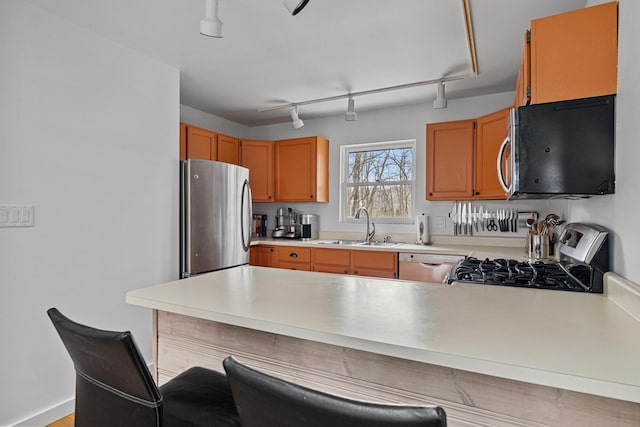 kitchen with stainless steel appliances, a peninsula, a sink, light countertops, and a kitchen bar