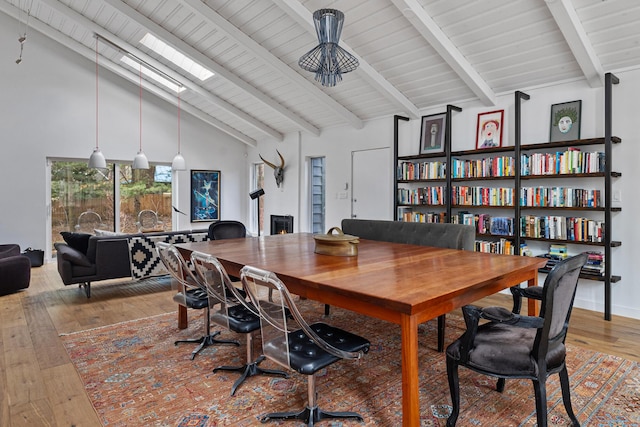 office featuring a warm lit fireplace, a skylight, hardwood / wood-style flooring, beamed ceiling, and high vaulted ceiling