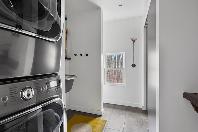 laundry room featuring stacked washer / drying machine, laundry area, baseboards, and tile patterned floors