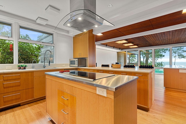 kitchen featuring black electric cooktop, a sink, light wood-type flooring, a center island, and stainless steel microwave