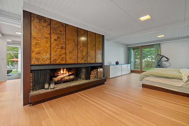 bedroom featuring access to outside, a warm lit fireplace, beamed ceiling, and wood finished floors