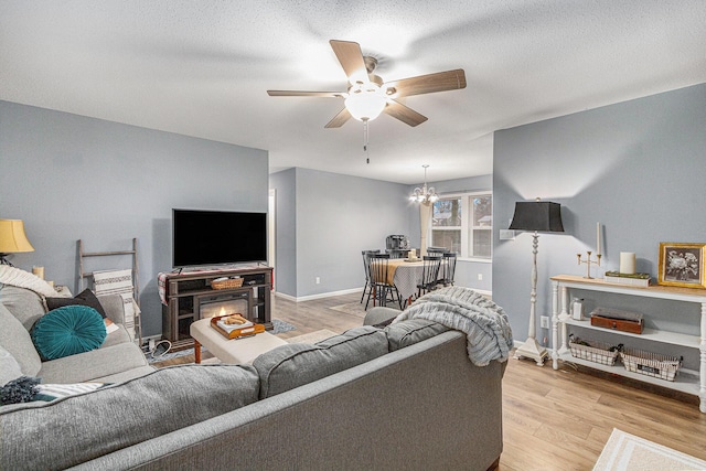 living room with ceiling fan with notable chandelier, light wood finished floors, a textured ceiling, and baseboards