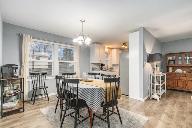 dining area featuring light wood-type flooring, a notable chandelier, and baseboards