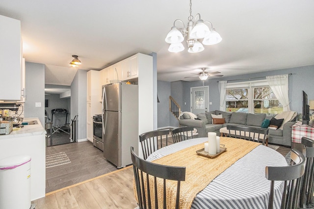 dining room featuring stairs, light wood finished floors, and ceiling fan with notable chandelier