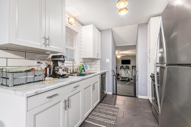 kitchen with tasteful backsplash, appliances with stainless steel finishes, a ceiling fan, white cabinets, and a sink