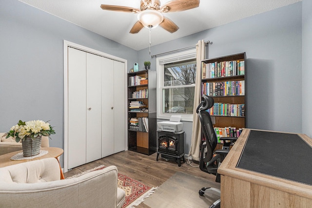 office area with a wood stove, ceiling fan, and wood finished floors