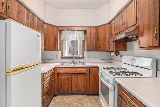 kitchen featuring white appliances, light countertops, a textured ceiling, under cabinet range hood, and a sink