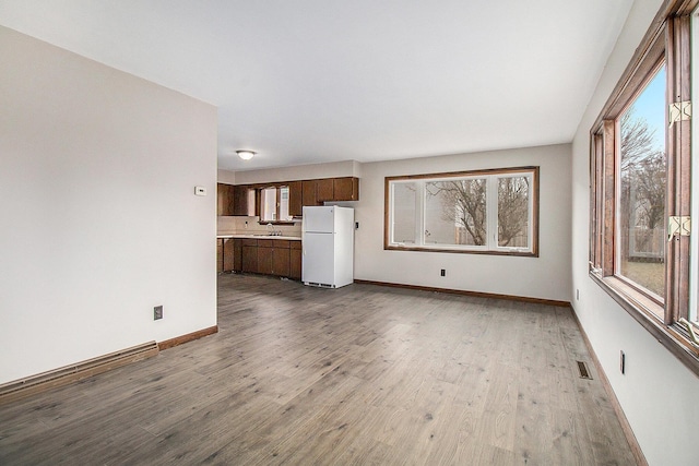 unfurnished living room with a wealth of natural light, baseboards, a sink, and wood finished floors