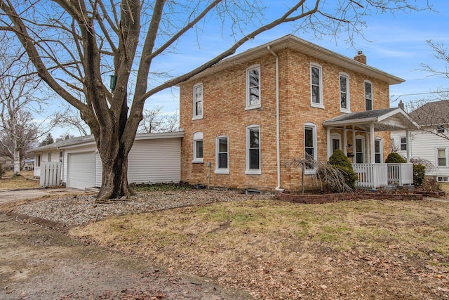 view of side of home featuring an attached garage, covered porch, brick siding, driveway, and a chimney