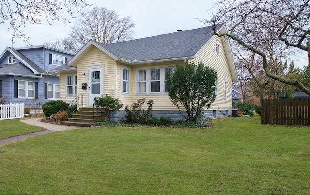 view of front of home with roof with shingles, fence, cooling unit, and a front yard