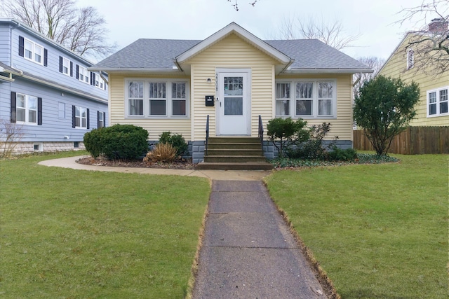 bungalow-style home featuring entry steps, roof with shingles, a front yard, and fence