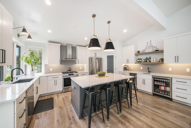 kitchen featuring wall chimney exhaust hood, wine cooler, appliances with stainless steel finishes, a breakfast bar, and a sink