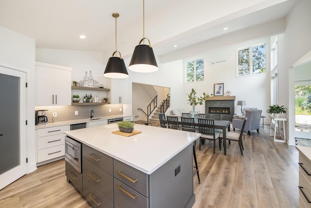 kitchen with white cabinets, a lit fireplace, light countertops, backsplash, and open shelves