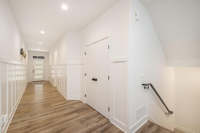 corridor with recessed lighting, a wainscoted wall, visible vents, an upstairs landing, and light wood-style floors