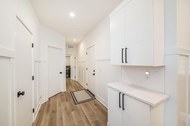 corridor featuring light wood finished floors, visible vents, a wainscoted wall, a decorative wall, and recessed lighting