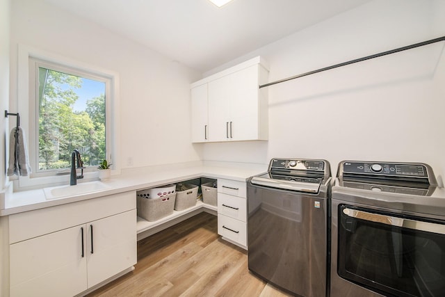 washroom featuring cabinet space, washer and clothes dryer, a sink, and light wood finished floors