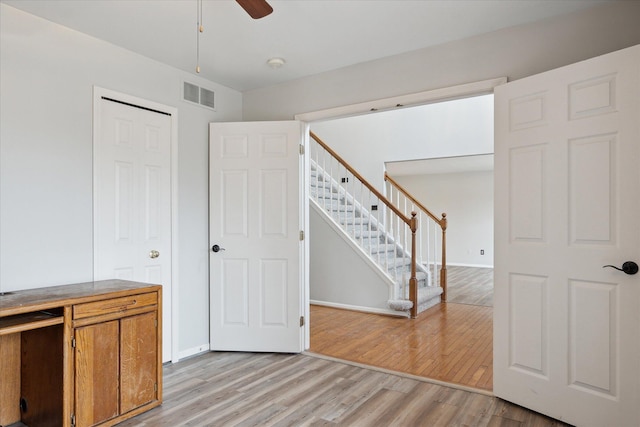 empty room with visible vents, light wood-style flooring, stairway, a ceiling fan, and baseboards