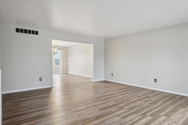 empty room with light wood finished floors, baseboards, visible vents, and a notable chandelier