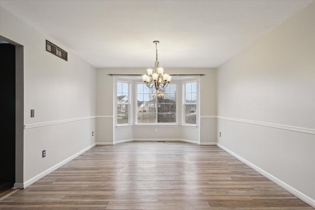 unfurnished dining area featuring a notable chandelier, baseboards, visible vents, and wood finished floors