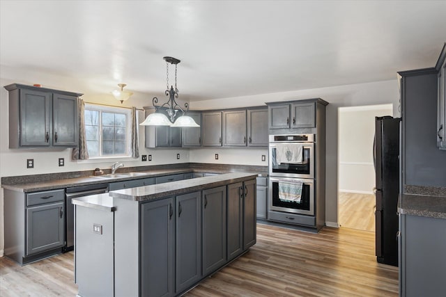 kitchen with dark countertops, stainless steel appliances, a sink, and wood finished floors