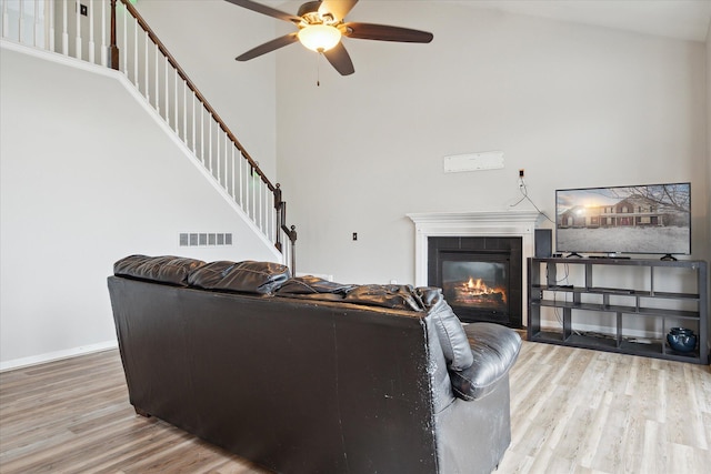 living area featuring a tile fireplace, wood finished floors, visible vents, baseboards, and stairway