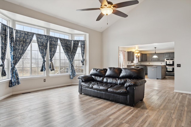 living room featuring high vaulted ceiling, ceiling fan with notable chandelier, visible vents, baseboards, and light wood finished floors