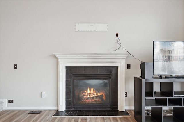 interior details featuring a tiled fireplace, wood finished floors, visible vents, and baseboards