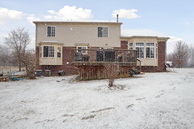 snow covered property with brick siding and a wooden deck