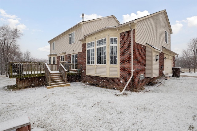 snow covered house with brick siding and a wooden deck