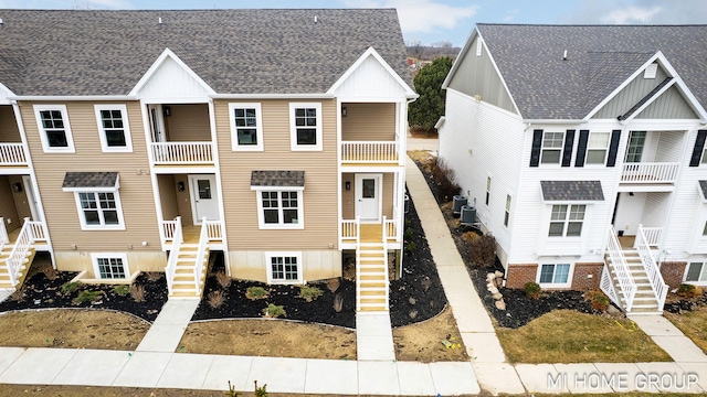 view of front facade with central AC unit, a shingled roof, and stairs