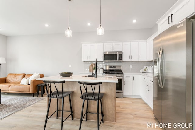 kitchen featuring light wood finished floors, a breakfast bar, light countertops, decorative backsplash, and appliances with stainless steel finishes