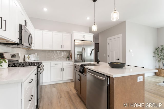 kitchen featuring light wood finished floors, a sink, tasteful backsplash, appliances with stainless steel finishes, and light countertops