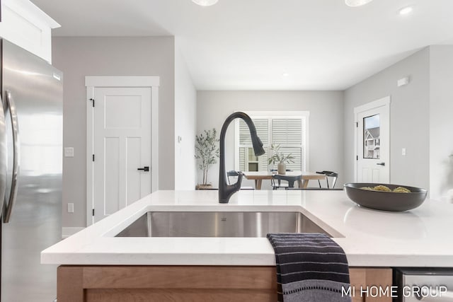 kitchen with light stone counters, white cabinets, freestanding refrigerator, and a sink