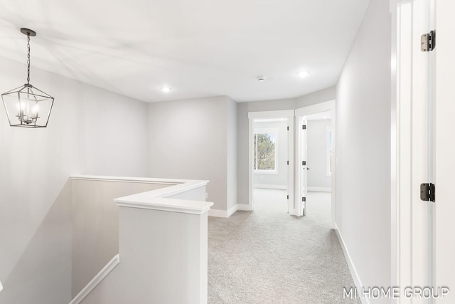 corridor with baseboards, an upstairs landing, light colored carpet, and a chandelier