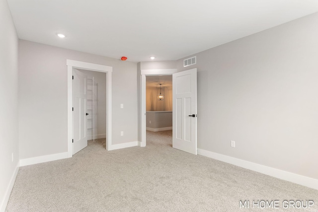 unfurnished bedroom with visible vents, light colored carpet, a walk in closet, and baseboards