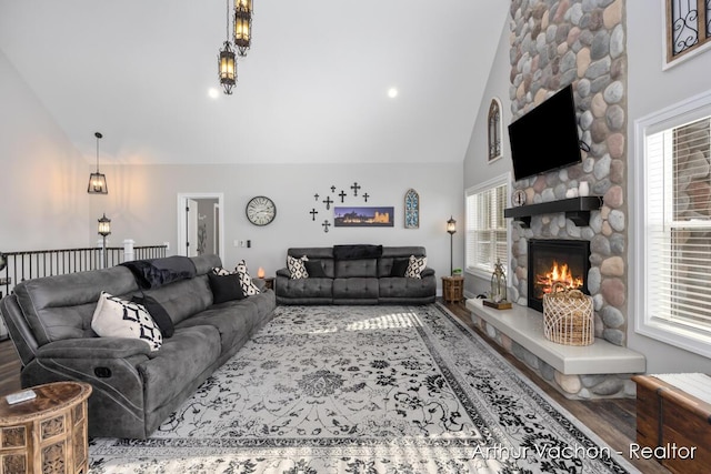 living room featuring high vaulted ceiling, wood finished floors, and a stone fireplace